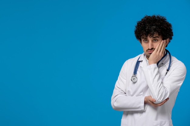 Dottori giorno ricci bel ragazzo carino in uniforme medica pensando in modo confuso