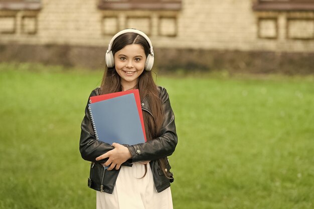 Dove la conoscenza incontra i moderni ausili per la formazione Il bambino felice indossa le cuffie moderne all'aperto La bambina ascolta la musica Vita moderna Nuova tecnologia Apprendimento moderno Scuola e istruzione