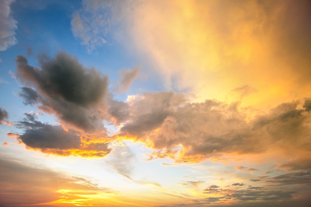 Drammatico paesaggio tramonto giallo con nuvole gonfie illuminate dal sole al tramonto arancione e cielo blu.