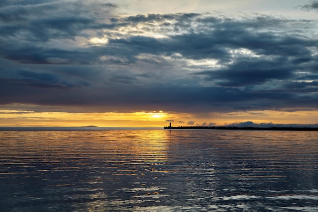 Drammatico tramonto con nuvole temporalesche prima della tempesta Molo sul mare con un faro sullo sfondo del sole al tramonto