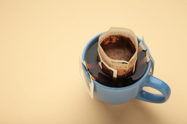 Drip coffee bag with ground coffee in cup on beige background