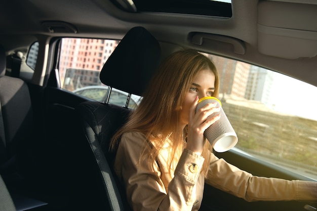 Driver di giovane donna che beve una tazza di caffè caldo in macchina in movimento.