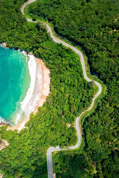 Drone aereo vista dall'alto verso il basso delle onde che si infrangono nella sabbia con strada e foresta Vista dall'alto