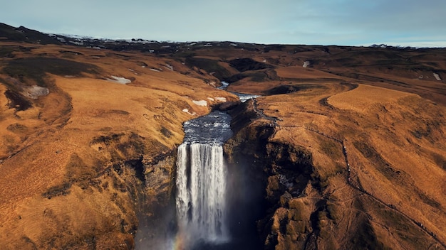 Drone scattato di una grande cascata in Islanda, un ruscello d'acqua che scende da bellissime scogliere marroni. Maestosa cascata islandese di skgafoss che cade dalle colline formando un paesaggio spettacolare.