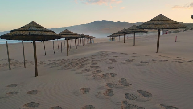 Drone veloce che vola ombrelli di paglia spiaggia primo piano tramonto paesaggio resort sabbioso