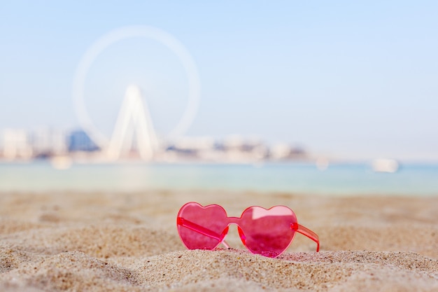 Dubai, Emirati Arabi Uniti, novembre 2019. Occhiali da sole rosa su una spiaggia sabbiosa con vista sull'Isola Bluewaters e sulla ruota panoramica di Dubai Eye, luna di miele, relax, spazio di copia