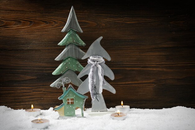 Due abeti, candele e casa nella neve su sfondo di legno, natura morta