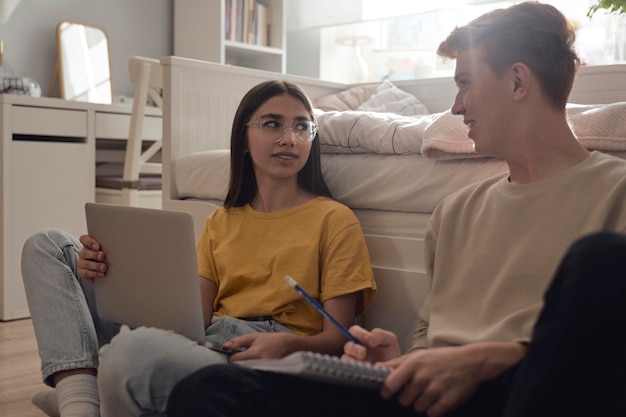 Due adolescenti caucasici seduti sul pavimento e che imparano dai libri e dal portatile