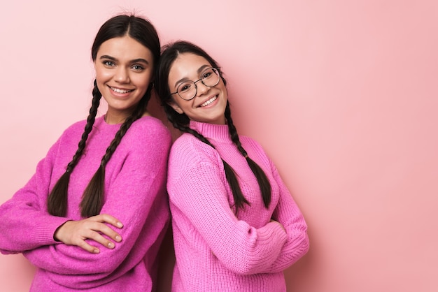 due adolescenti felici con le trecce in abiti casual che sorridono alla telecamera isolata su un muro rosa