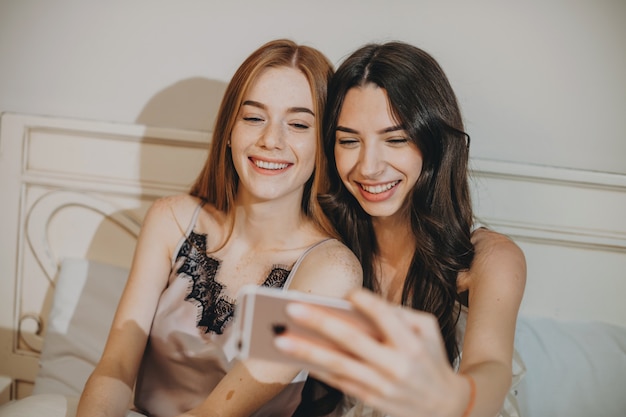 Due adorabili sorelle in pijama ridono mentre fanno un selfie a letto.