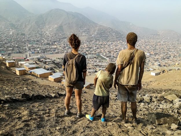 Due adulti e un bambino osservano una città in lontananza con vestiti sporchi, paesaggio apocalittico