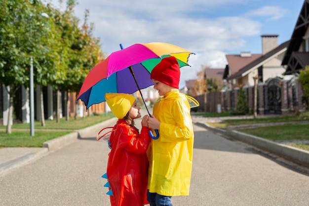 Due affascinanti bambini un ragazzo e una ragazza giocano nel parco con un ombrello colorato