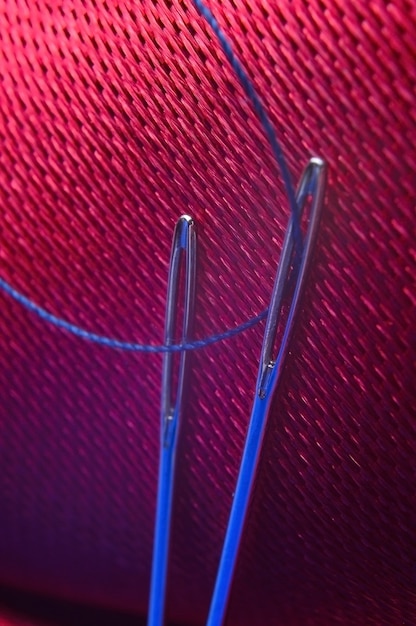 Due aghi da cucito con filo blu su uno sfondo di tessuto rosso. avvicinamento.