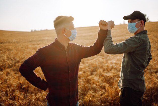 Due agricoltori in maschere mediche sterili con tablet in mano nel campo di grano controllano la qualità del raccolto