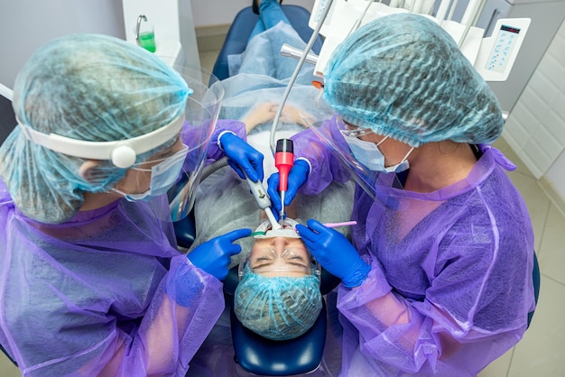 Due aiutanti in abiti speciali maschere cappelli guanti aiutano a condurre l'operazione dal dentista