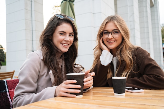 Due allegre amiche attraenti sedute al bar all'aperto, bevendo caffè