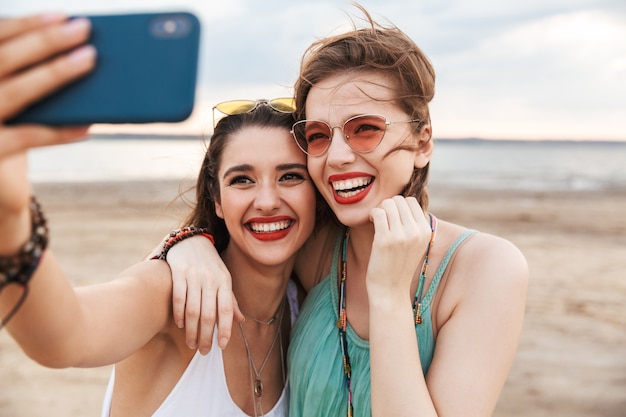 Due allegre amiche che trascorrono del tempo in spiaggia, ridendo, facendo un selfie