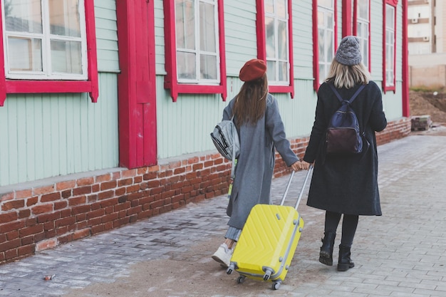 Due allegre donne turistiche che sorridono e camminano con le valigie sulla strada della città in autunno o primavera tim