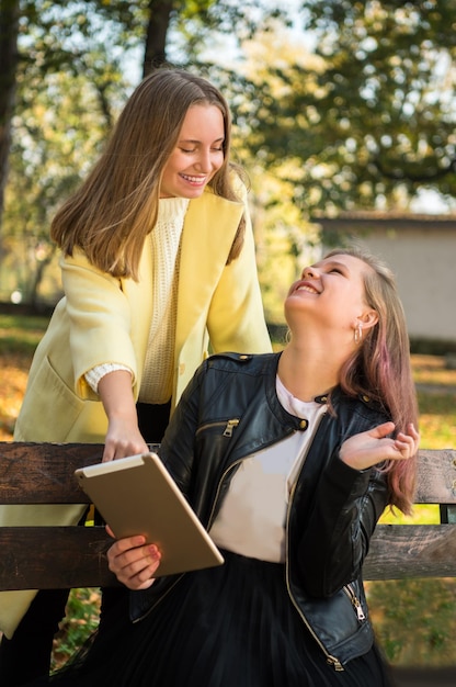 Due allegre migliori amiche in abbigliamento casual utilizzando tablet nel parco soleggiato autunnale Ragazze adolescenti felici all'aperto