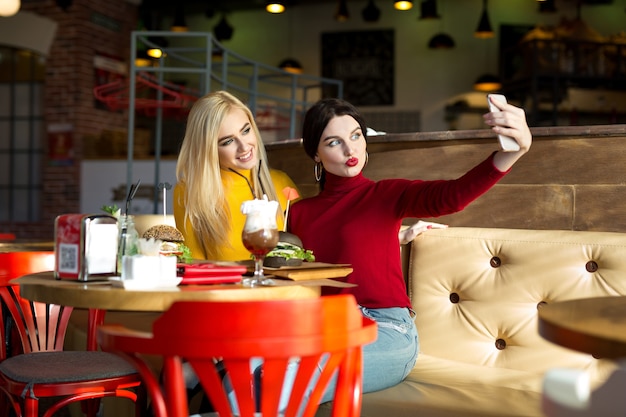 Due allegre ragazze allegre che prendono un selfie seduti insieme al caffè