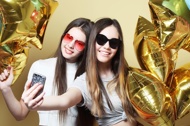 Due amiche adolescenti con palloncini d'oro fanno selfie su un p