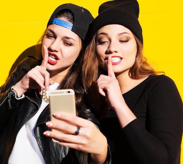 Due amiche adolescenti in abito hipster all'aperto fanno selfie su un telefono