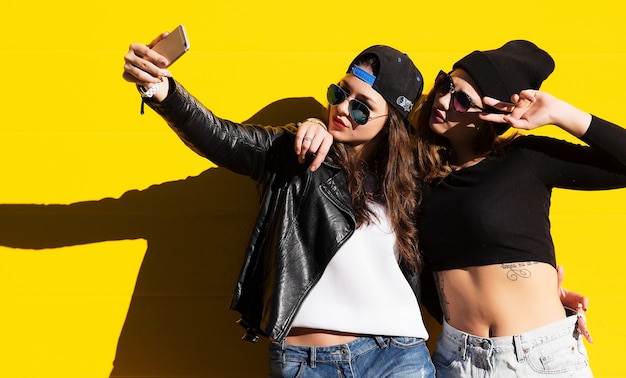 Due amiche adolescenti in abito hipster all'aperto fanno selfie su un telefono