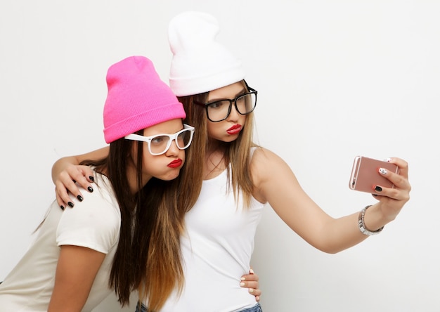 Due amiche adolescenti in abito hipster fanno selfie su un telefono.