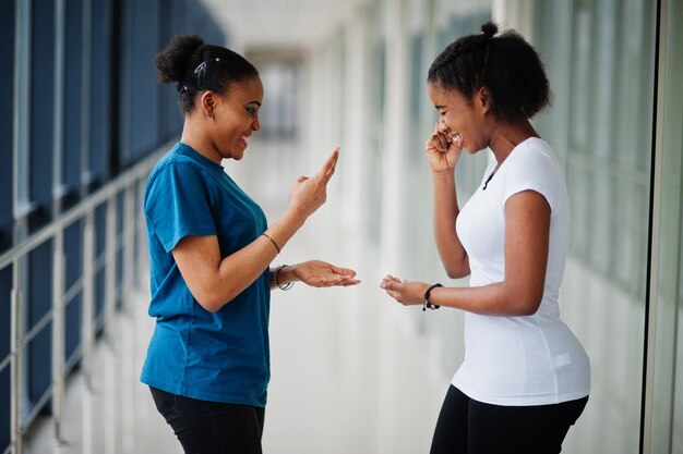 Due amiche africane in t-shirt giocano insieme a forbici di carta rock al coperto.