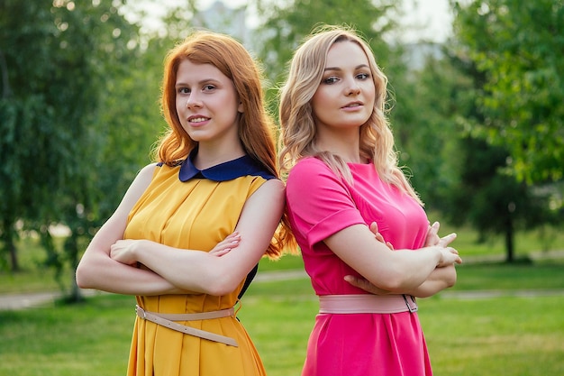 Due amiche allegre attive bella giovane ragazza irlandese rossa rossa con un vestito giallo e una donna bionda europea in un vestito rosa che parla nel parco estivo. incontrare due amiche