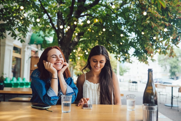 Due amiche che navigano nei telefoni cellulari al caffè di strada