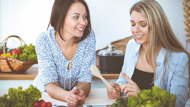 Due amiche che scelgono la ricetta per un pasto delizioso seduti al tavolo in cucina Tablet pc è il miglior libro di cucina