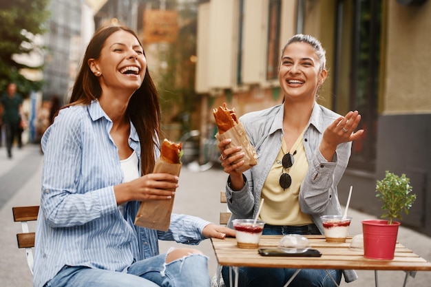 Due amiche che si divertono all'aperto mangiando panini