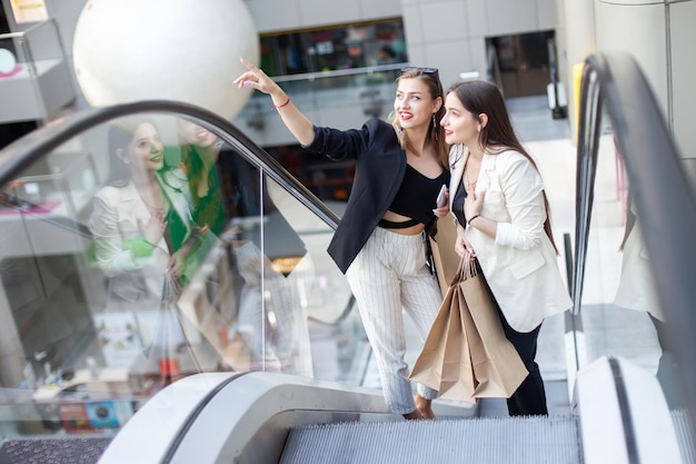 Due amiche con le borse della spesa salgono sulla scala mobile nel centro commerciale