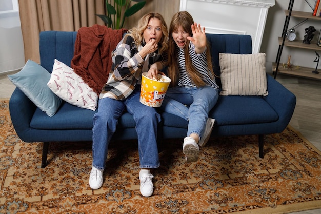 Due amiche con un'espressione spaventata che guardano la tv e mangiano popcorn