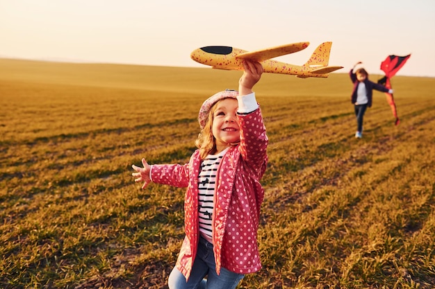 Due amiche di bambine si divertono insieme con l'aquilone e l'aereo giocattolo sul campo durante il giorno soleggiato