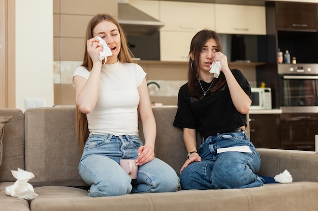 Due amiche emotive che guardano un melodramma in TV e piangono mentre sono sedute sul divano