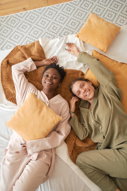 Due amiche felici in un comodo pigiama di mussola naturale sono sdraiate a letto