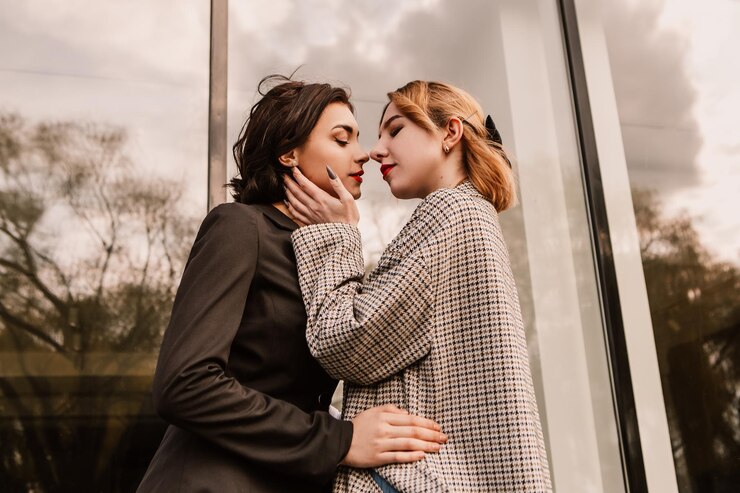 Due amiche graziose che posano vicino all'edificio di vetro. Coppia di ragazze lesbiche gay che abbracciano l'abbraccio