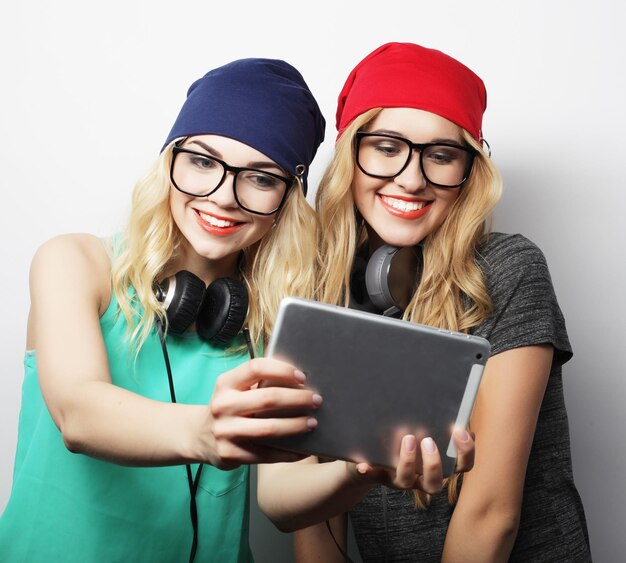 Due amiche hipster che si fanno un selfie con un tablet digitale. Studio girato su Grey Waccground.