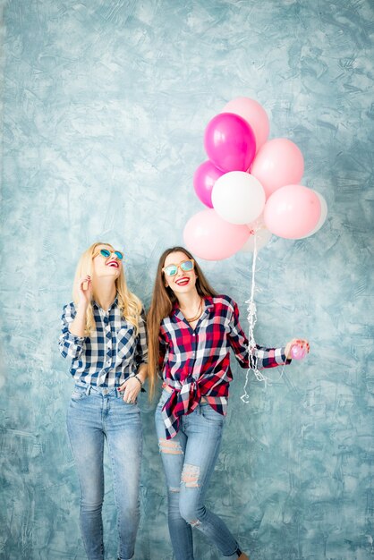 Due amiche in camicie a scacchi si divertono con i palloni ad aria sullo sfondo della parete blu