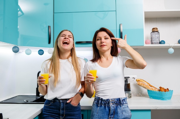 Due amiche in piedi in cucina e bevono succo d'arancia. Le amiche chiacchierano e condividono segreti in cucina, a colazione