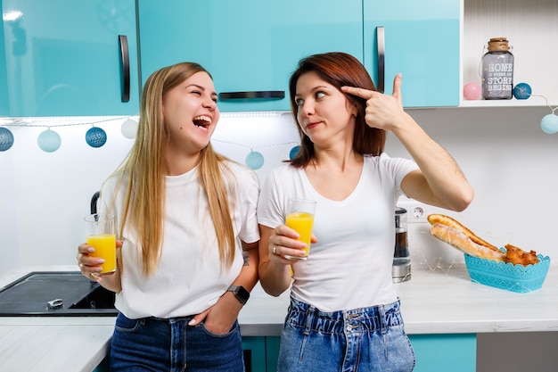 Due amiche in piedi in cucina e bevono succo d'arancia. Le amiche chiacchierano e condividono segreti in cucina, a colazione