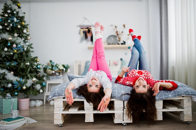 Due amiche indossano maglioni invernali divertirsi sul letto in camera con decorazioni di Natale.
