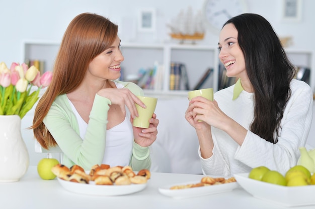 Due amiche sorridenti che si siedono al tavolo e che bevono tè