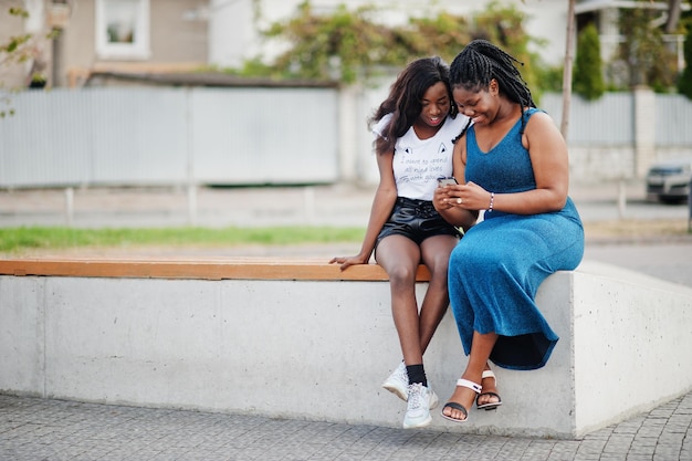 Due amici afroamericani dalla pelle scura femminile Uno di loro più il modello di taglia seconda sottile Divertirsi e trascorrere del tempo insieme Guarda il telefono cellulare