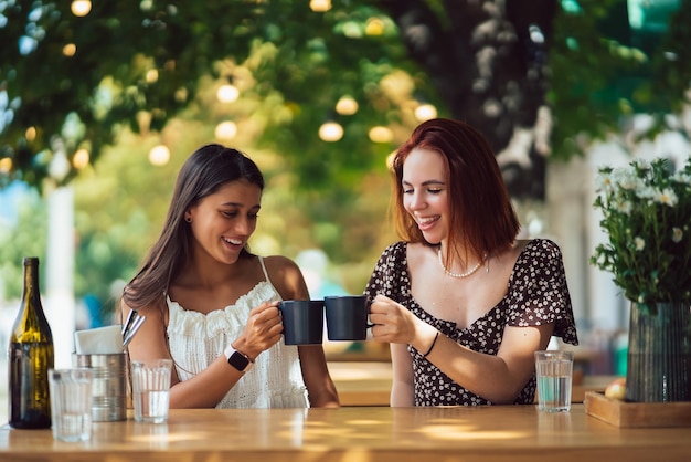 Due amici che bevono caffè donne che tintinnano con tazze di caffè