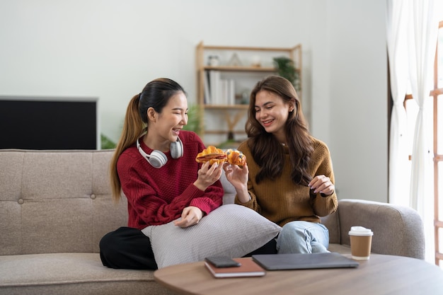 Due amici che si divertono a mangiare un croissant seduti su un divano nel soggiorno di casa