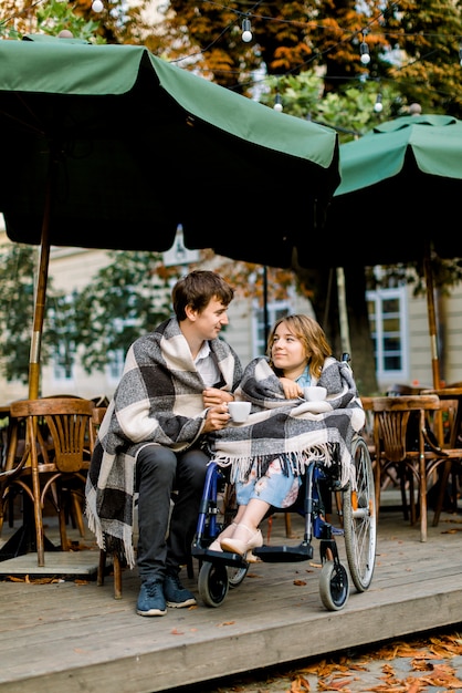 Due amici, coppia adorabile uomo e donna coperti di plaid a scacchi in un caffè all'aperto a bere il caffè