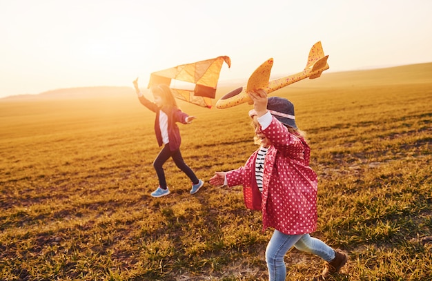 Due amici di bambine si divertono insieme con l'aquilone e l'aereo giocattolo sul campo durante il giorno soleggiato